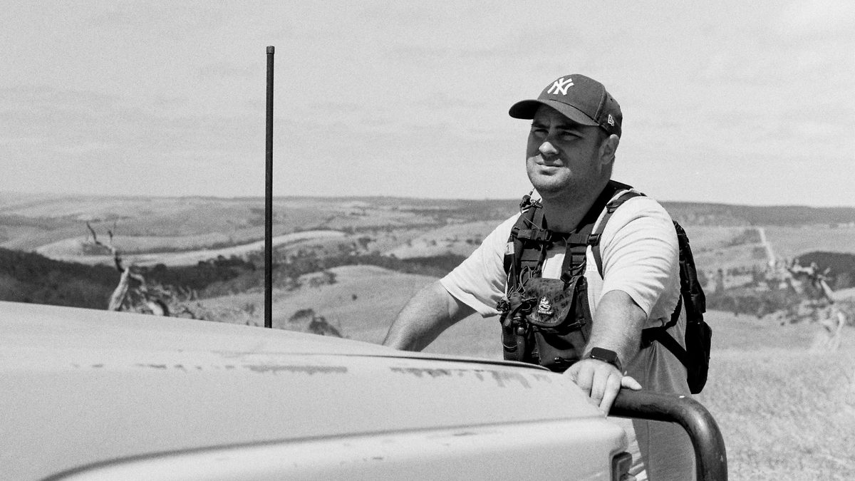 JVC the AD on location, leaning on a dusty ute above rolling hills, wearing a radio harness